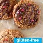 Four golden brown cookies on a sheet of brown baking paper with two drizzled with melted dark chocolate and sprinkled with freeze-dried raspberries