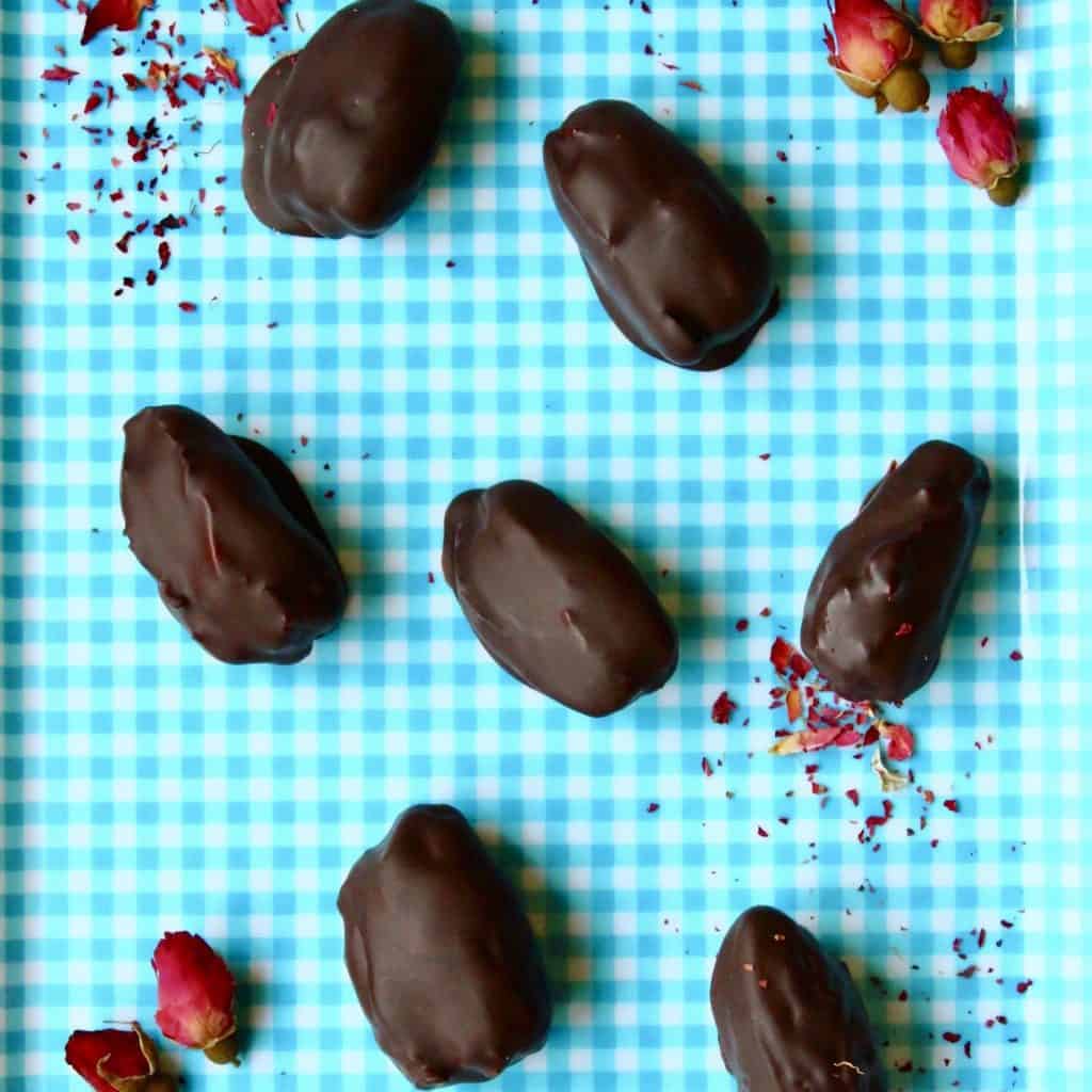 Seven chocolate-covered dates on a blue chequered background scattered with dried roses