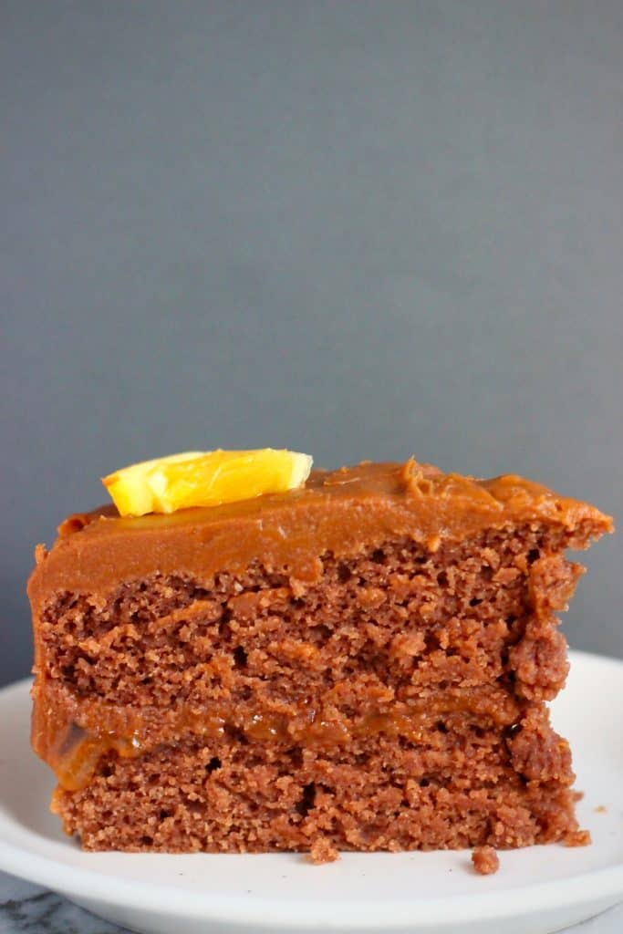 Photo of a slice of chocolate sponge sandwiched with chocolate frosting topped with a slice of orange against a dark grey background