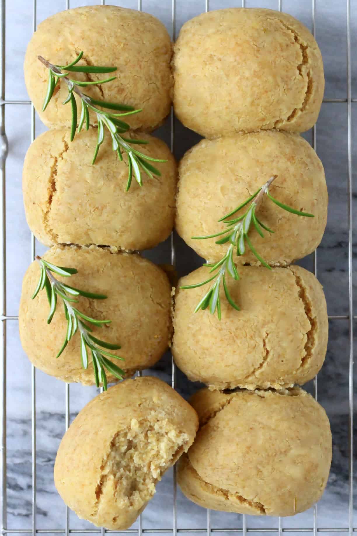 Eight gluten-free dinner rolls on a wire rack with a bite taken out of one