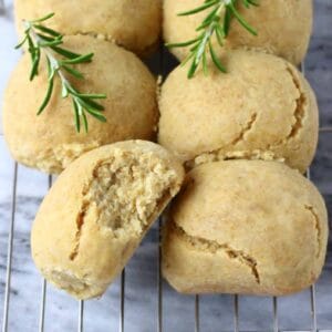 Six gluten-free dinner rolls on a wire rack with a bite taken out of one