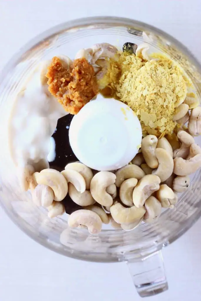 Cashew nuts, nutritional yeast, miso and yogurt in a food processor against a white background