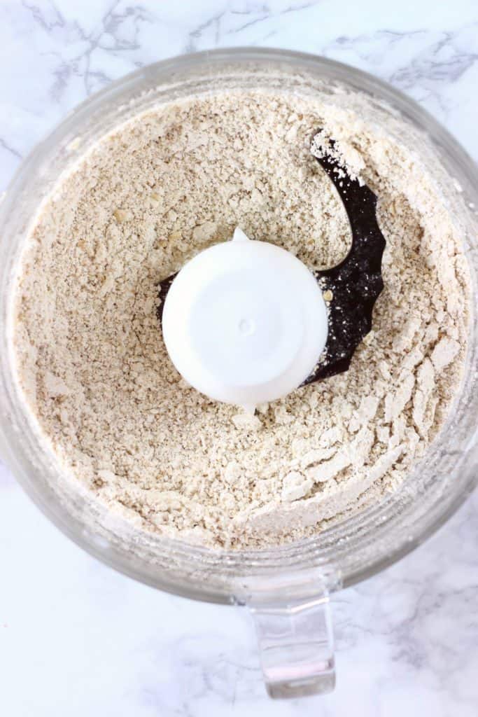 Oat flour in a food processor against a marble background
