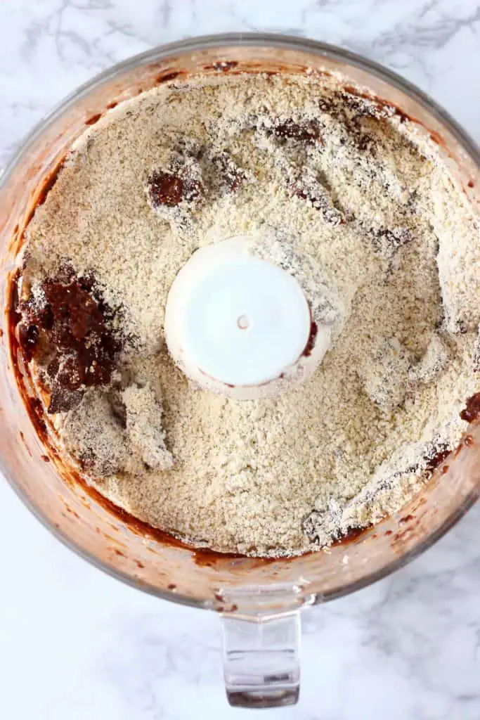 Chocolate sauce and oat flour in a food processor against a marble background