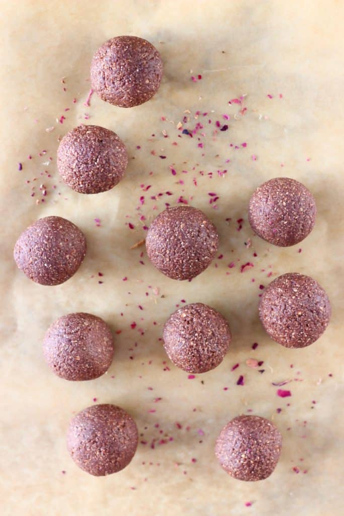 Ten chocolate brownie bites on a sheet of brown baking paper sprinkled with rose petals