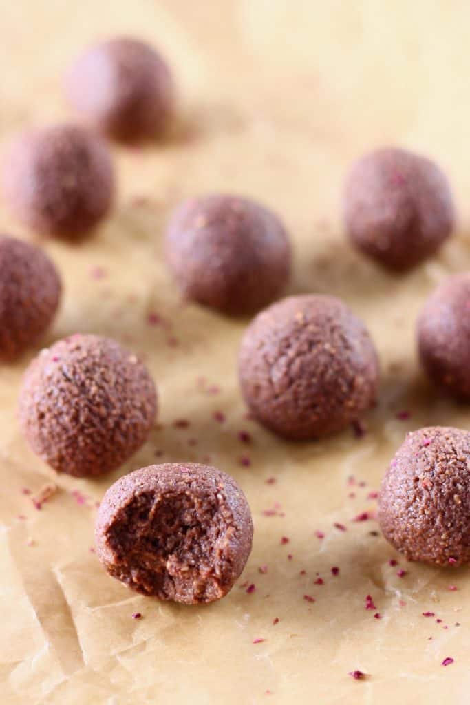 Ten chocolate balls one with bit taken out of it on a sheet of brown baking paper