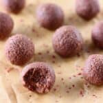 Ten chocolate balls one with bit taken out of it on a sheet of brown baking paper
