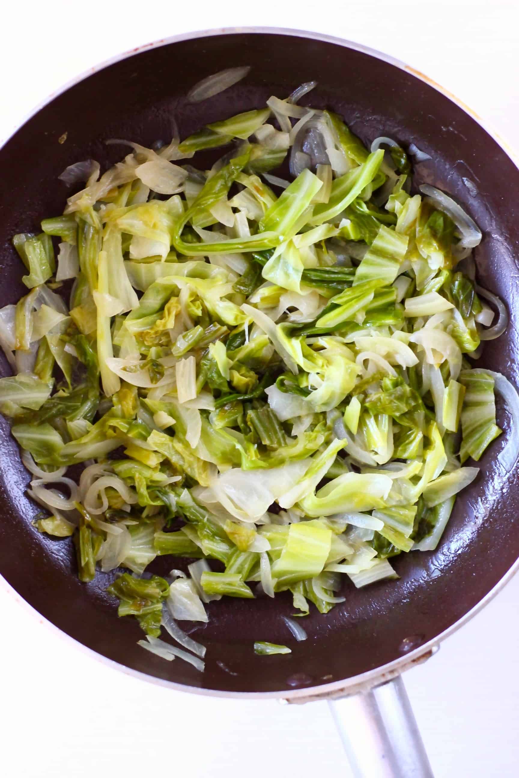 Sliced onions and cabbage being fried in a frying pan