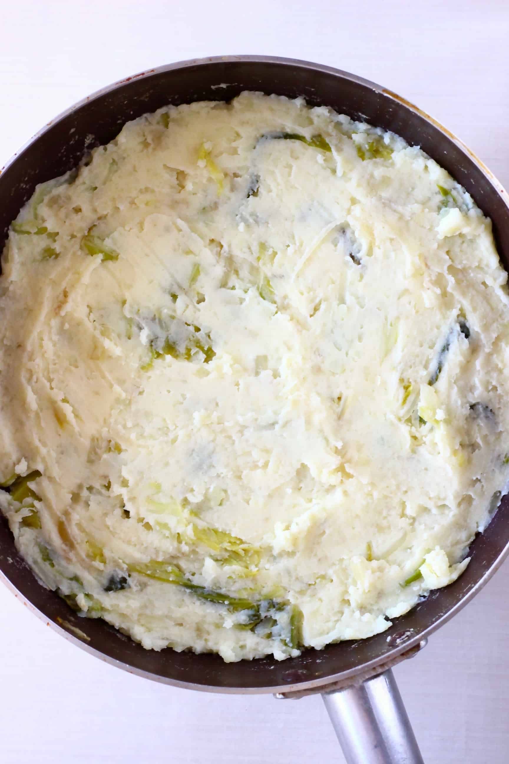 A raw bubble and squeak cake made with mashed potatoes and vegetables in a frying pan 