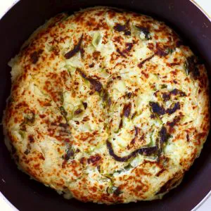 A circular, golden brown bubble and squeak cake in a frying pan