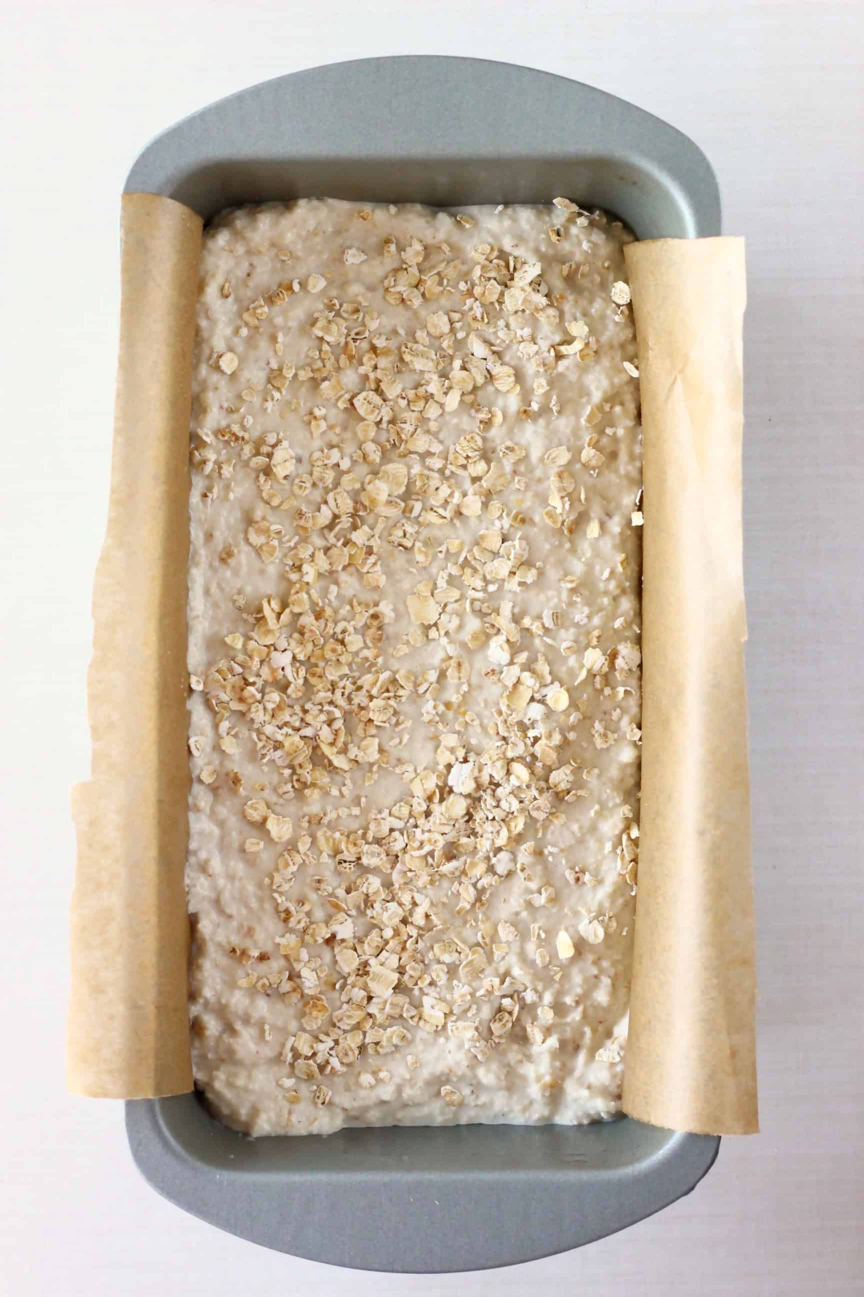 This Gluten-Free Vegan Oat Bread is soft on the inside, crusty on the outside, nutty, slightly chewy, and unbelievably easy to make! It's also no-knead, yeast-free and completely free from sugar! It's made in one bowl using simple ingredients, slices well and is perfect for making sandwiches! Dairy-free, soy-free, oil-free, corn-free, egg-free and nut-free optional. #rhiansrecipes #baking #bread #glutenfree #yeastfree #vegan #dairyfree #eggfree Gluten-free vegan oat bread dough sprinkled with oats in a loaf tin lined with baking paper