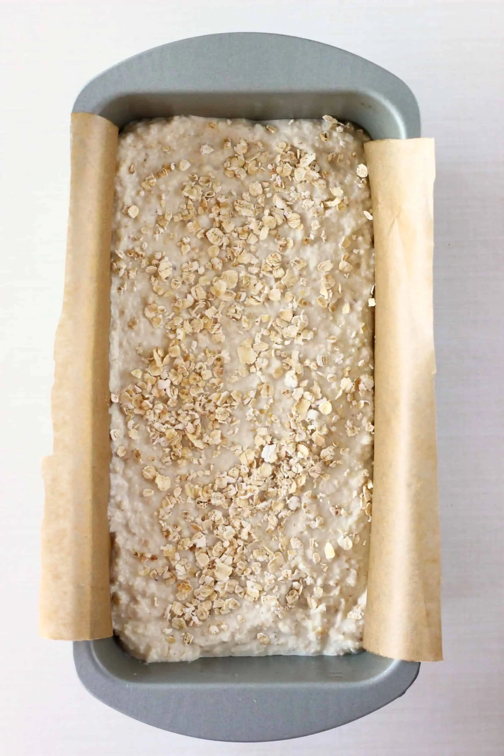 Gluten-free vegan oat bread dough sprinkled with oats in a loaf tin lined with baking paper 