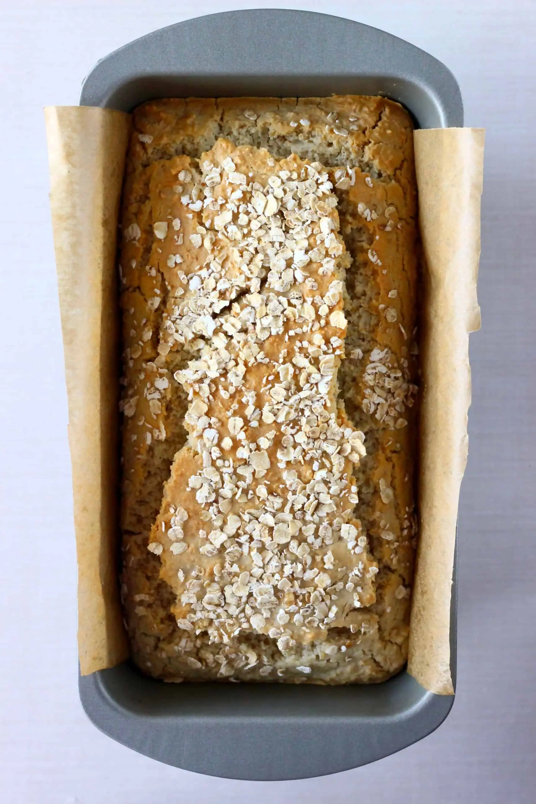 A loaf of gluten-free vegan oat bread topped with oats in a loaf tin