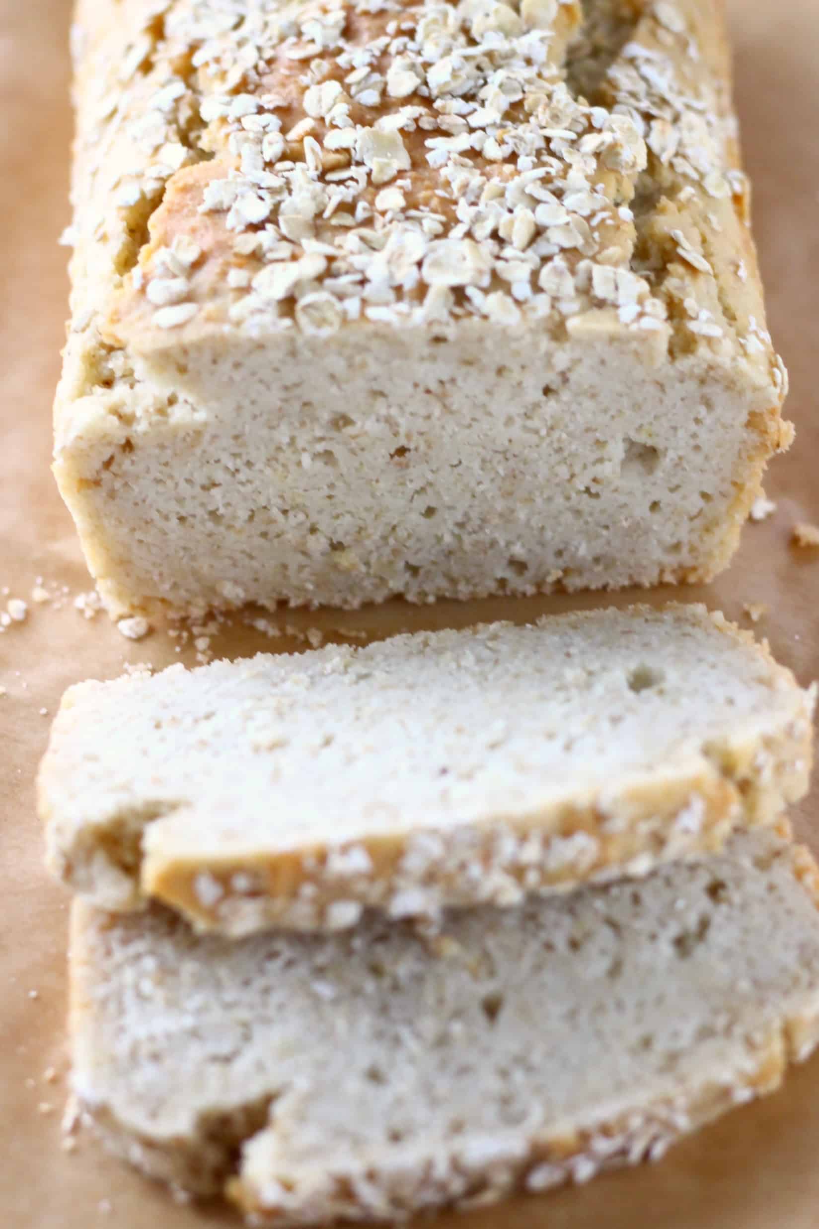 A loaf of gluten-free vegan oat bread topped with oats with two slices next to it