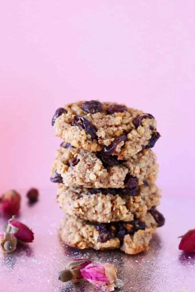 Four oatmeal raisin cookies stacked on top of each other against a pink background