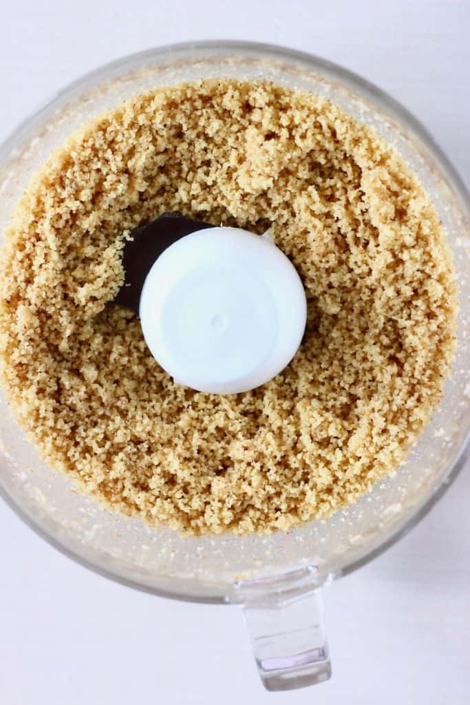 Ground walnuts in a food processor against a white background