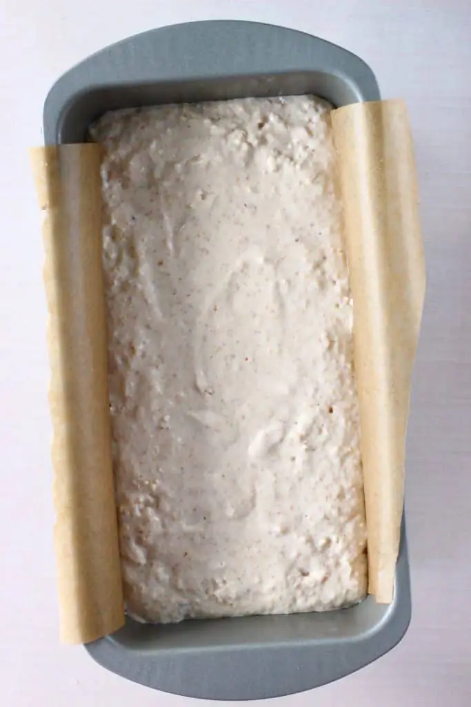 White bread batter in a silver loaf tin lined with brown baking paper against a white background