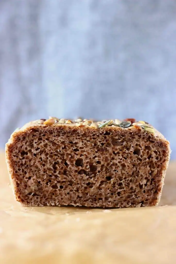 A sliced loaf of brown bread on a sheet of brown baking paper against a grey background