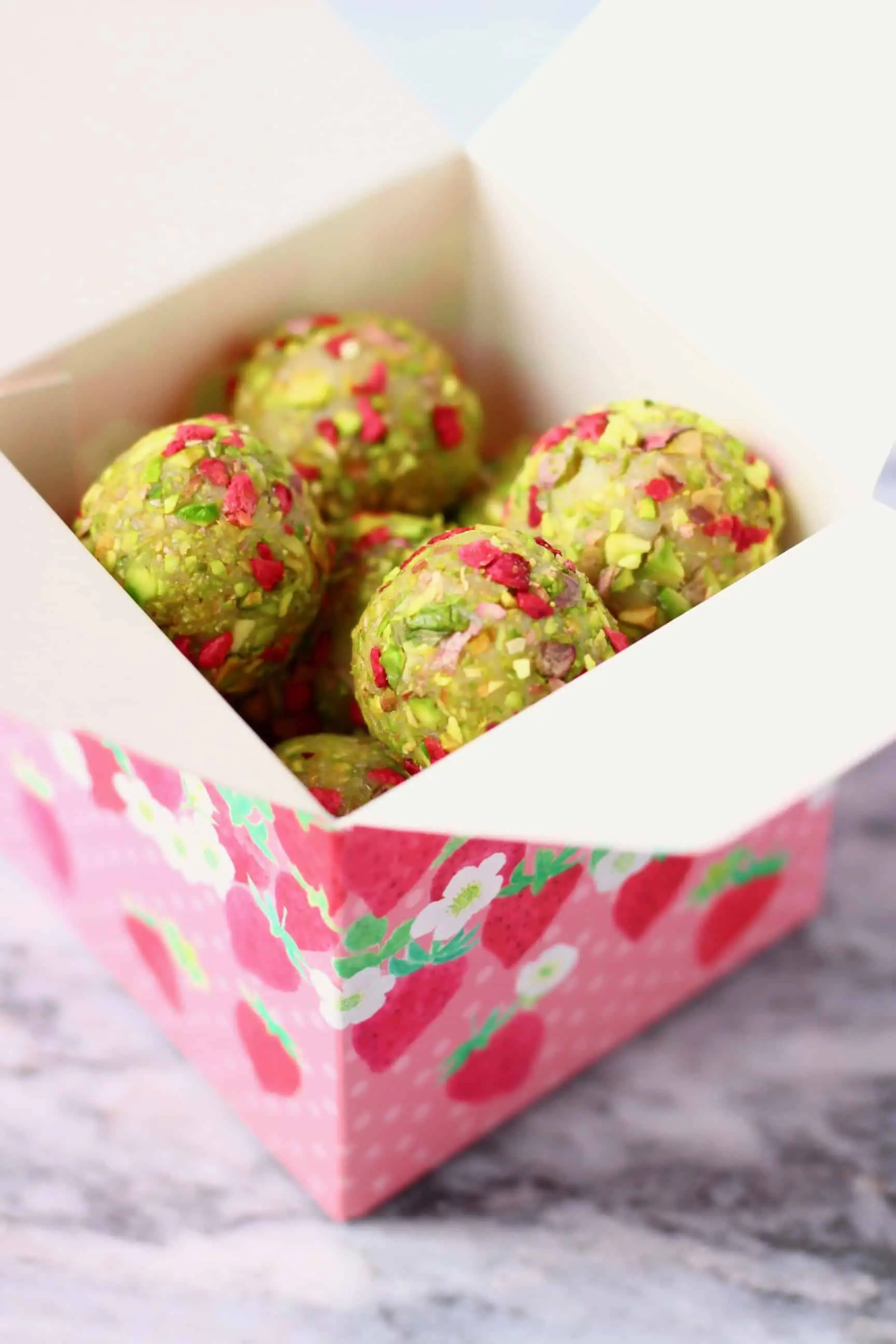 Vegan white chocolate truffles covered with chopped pistachios and freeze-dried raspberries in a small pink gift box 