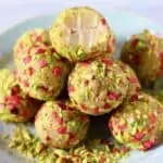 A pile of vegan white chocolate truffles covered in chopped pistachios and freeze-dried raspberries with a bitten one on top