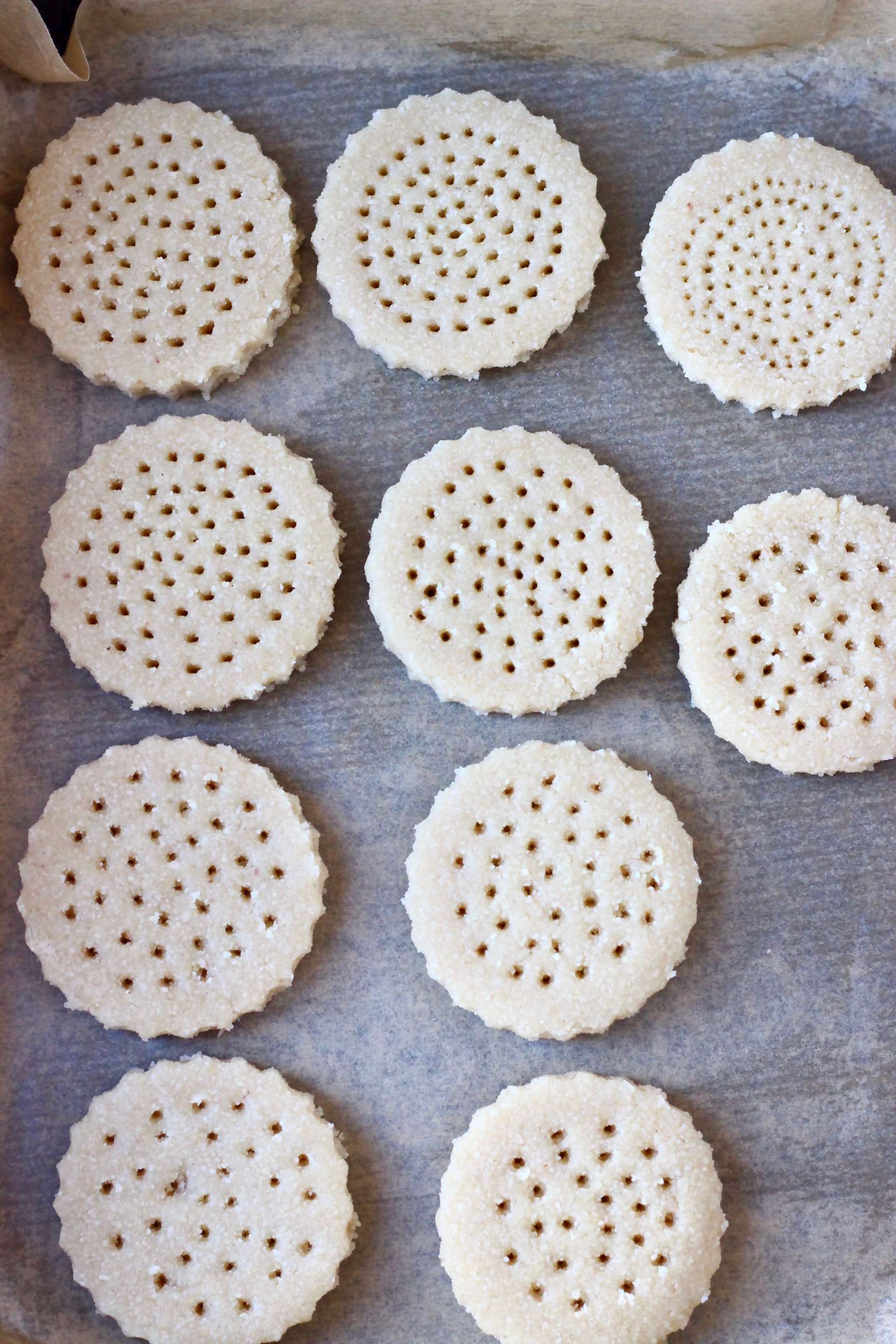Ten raw vegan shortbread cookies with holes cut out on baking paper