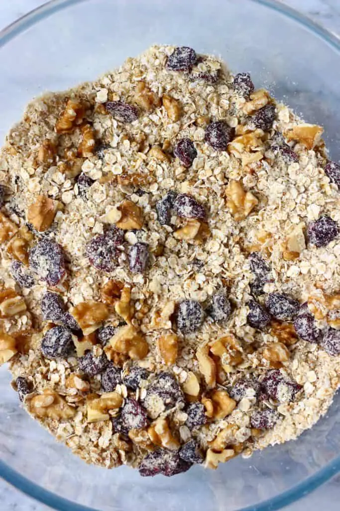 Oats, dried cranberries and chopped walnuts in a glass mixing bowl against a marble background