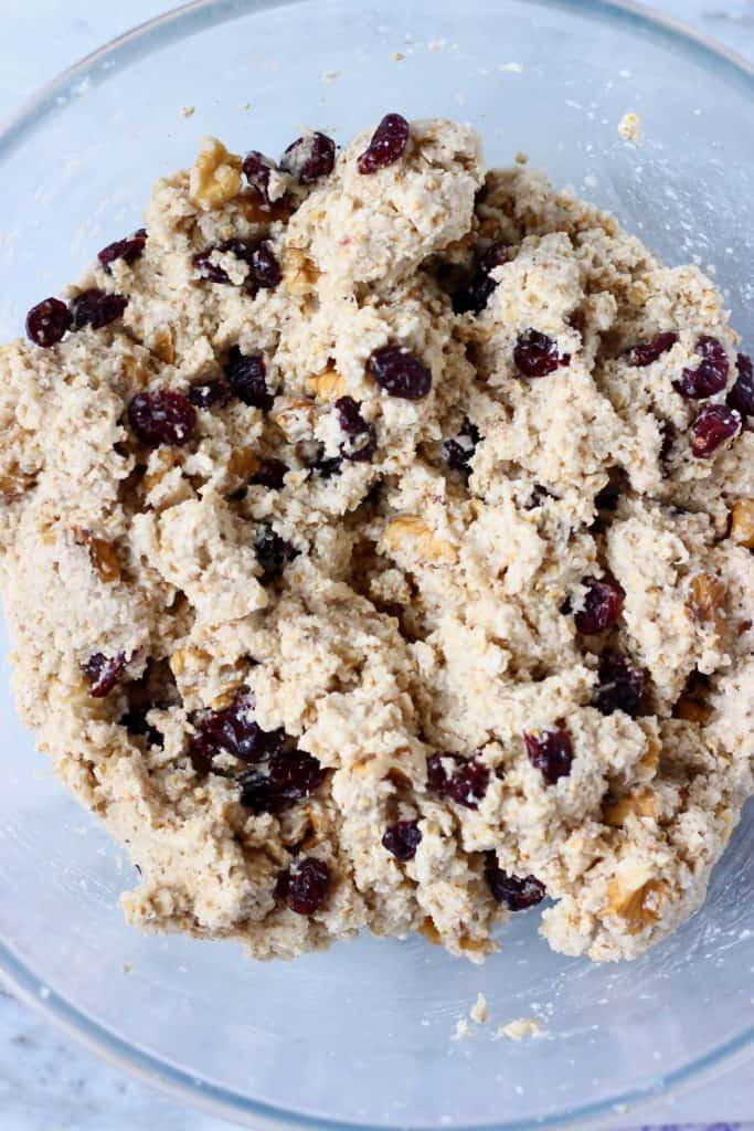 Raw oatmeal bread batter with cranberries and chopped walnuts in a glass mixing bowl against a marble background