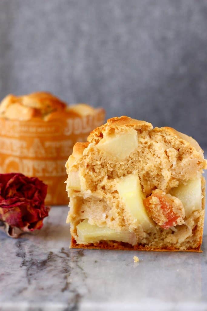 Photo of half a muffin with apples and another muffin on a marble slab against a grey background