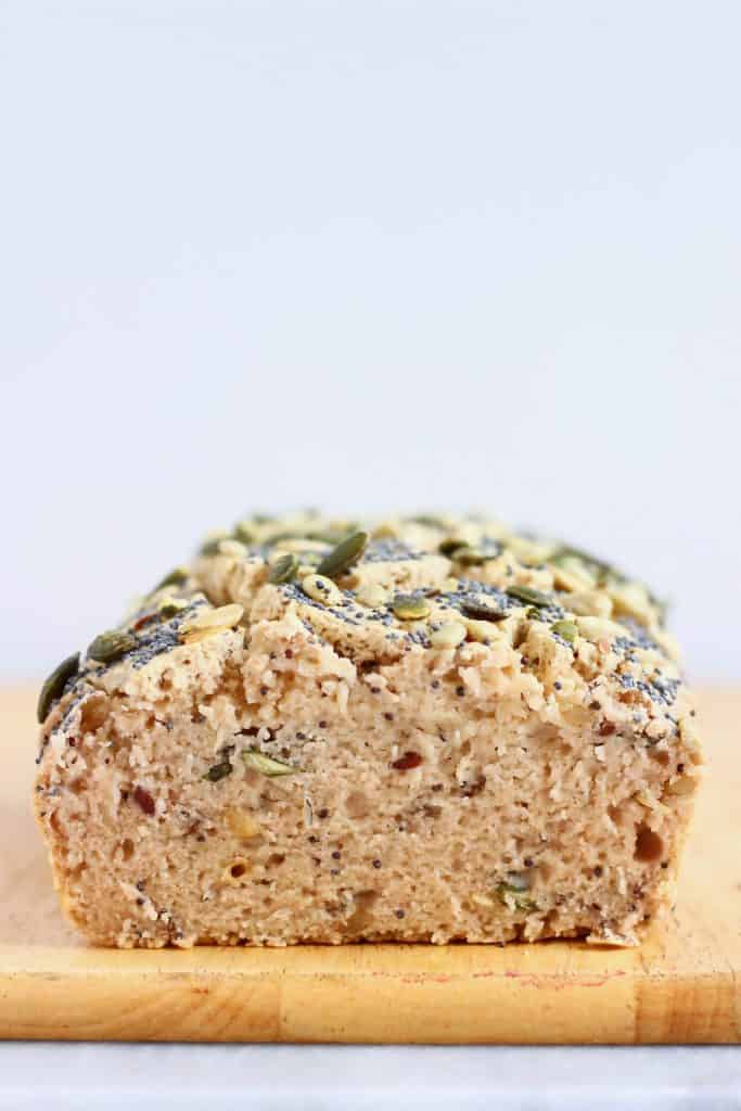 Photo of a sliced loaf of brown seeded bread on a light brown chopping board against a white background