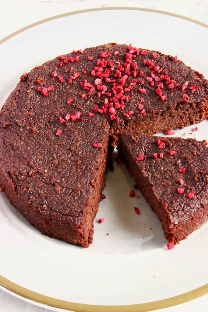 A chocolate cake with a slice taken out of it sprinkled with freeze-dried raspberries on a grey plate