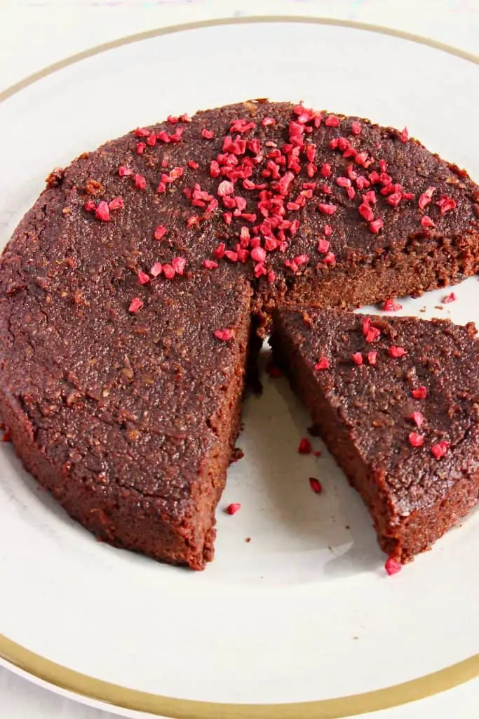 A chocolate cake with a slice taken out of it sprinkled with freeze-dried raspberries on a grey plate