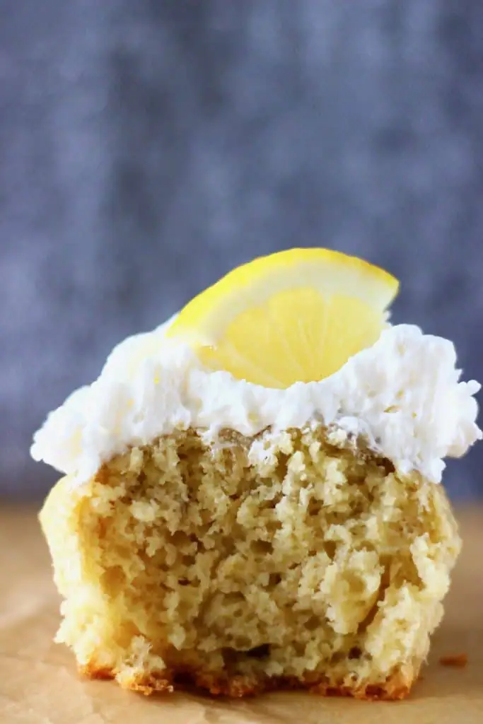 A yellow cupcake topped with white creamy frosting and a lemon wedge against a grey background