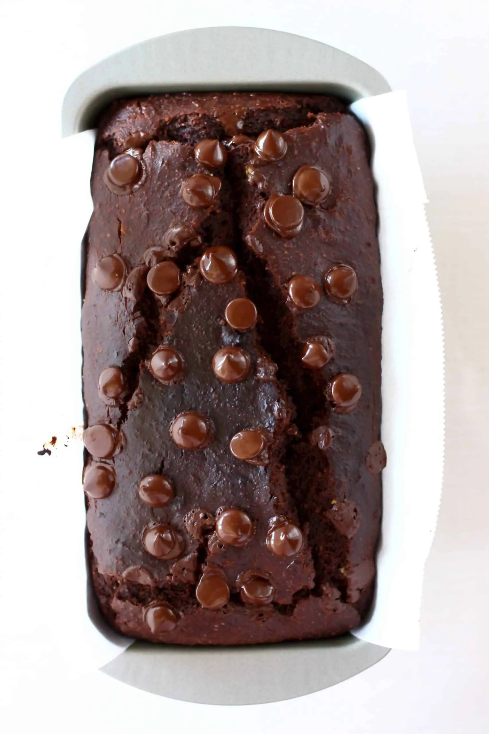A loaf of baked gluten-free vegan chocolate banana bread topped with chocolate chips in a loaf tin
