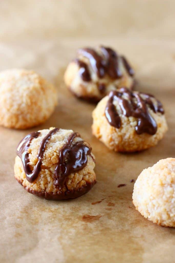 Five coconut macaroons drizzled with melted chocolate on a sheet of brown baking paper