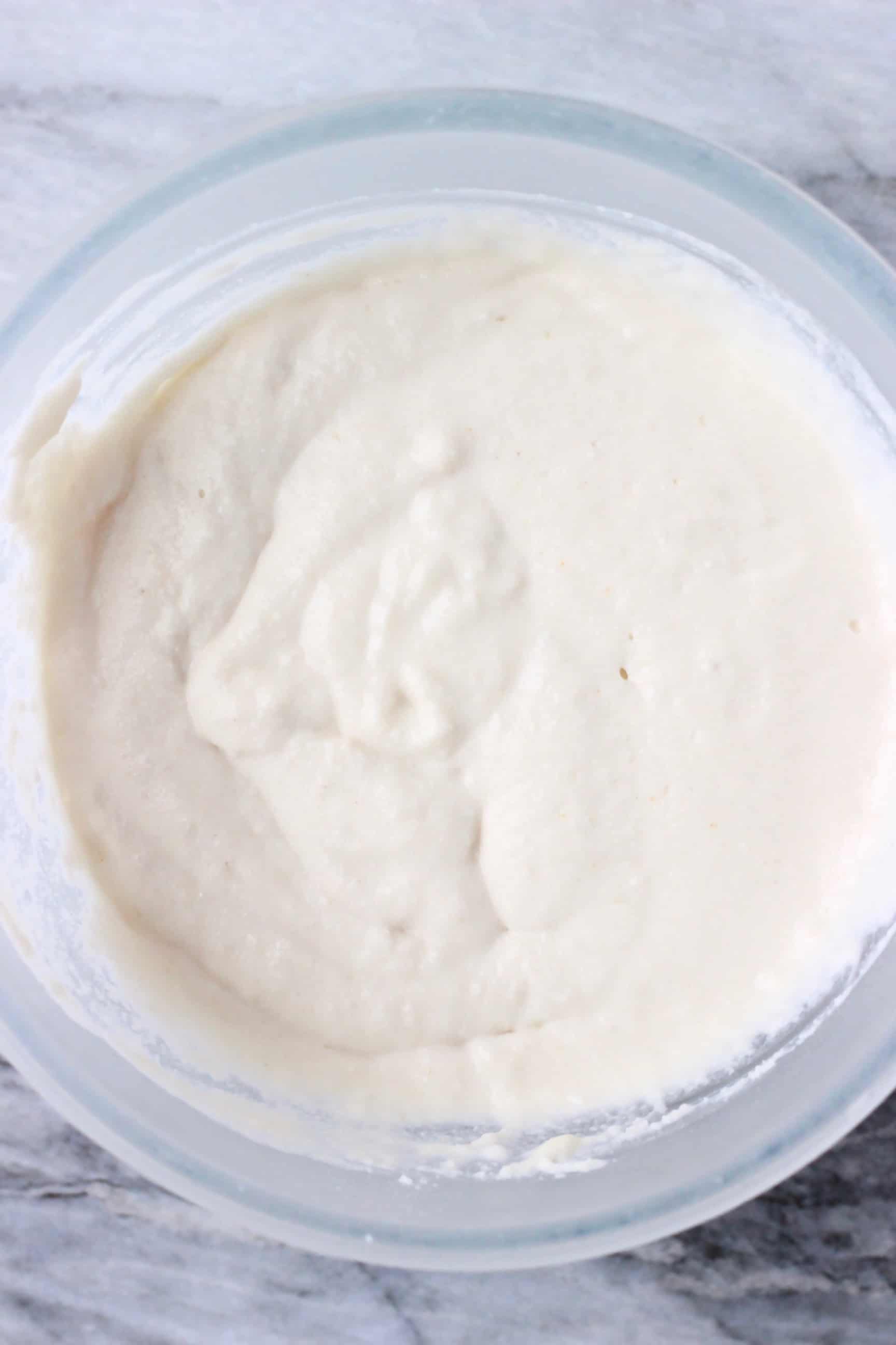 These Gluten-Free Vegan Coconut Flour Pancakes are fluffy, perfectly soft and chewy, and super easy to make. They make the best satisfying and nutritious breakfast! Dairy-free, refined sugar free, egg-free. #rhiansrecipes #pancakes #glutenfree #vegan #coconutflour #dairyfree Raw white vegan coconut flour pancake batter in a glass mixing bowl against a marble background