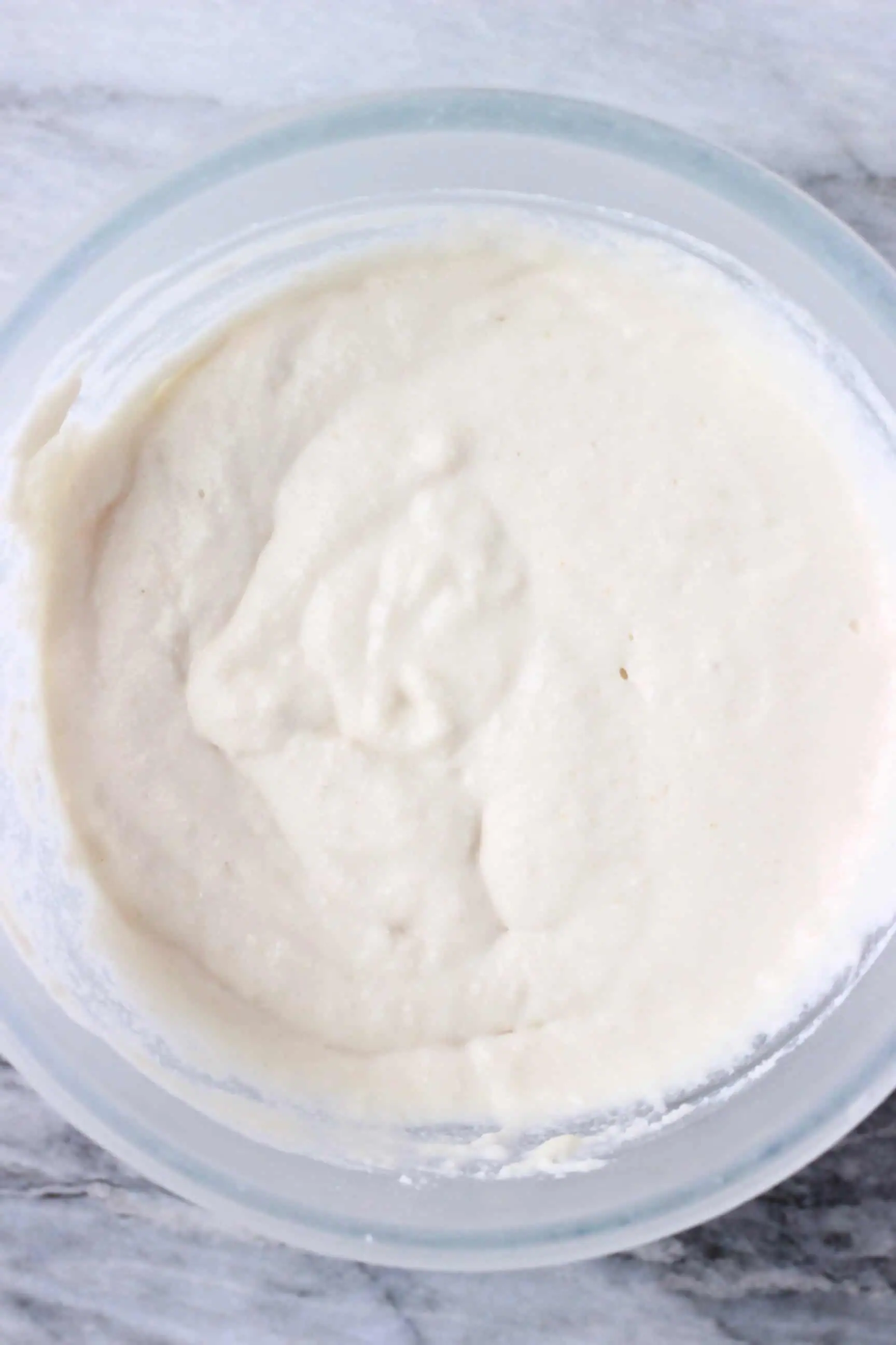 Raw white vegan coconut flour pancake batter in a glass mixing bowl against a marble background
