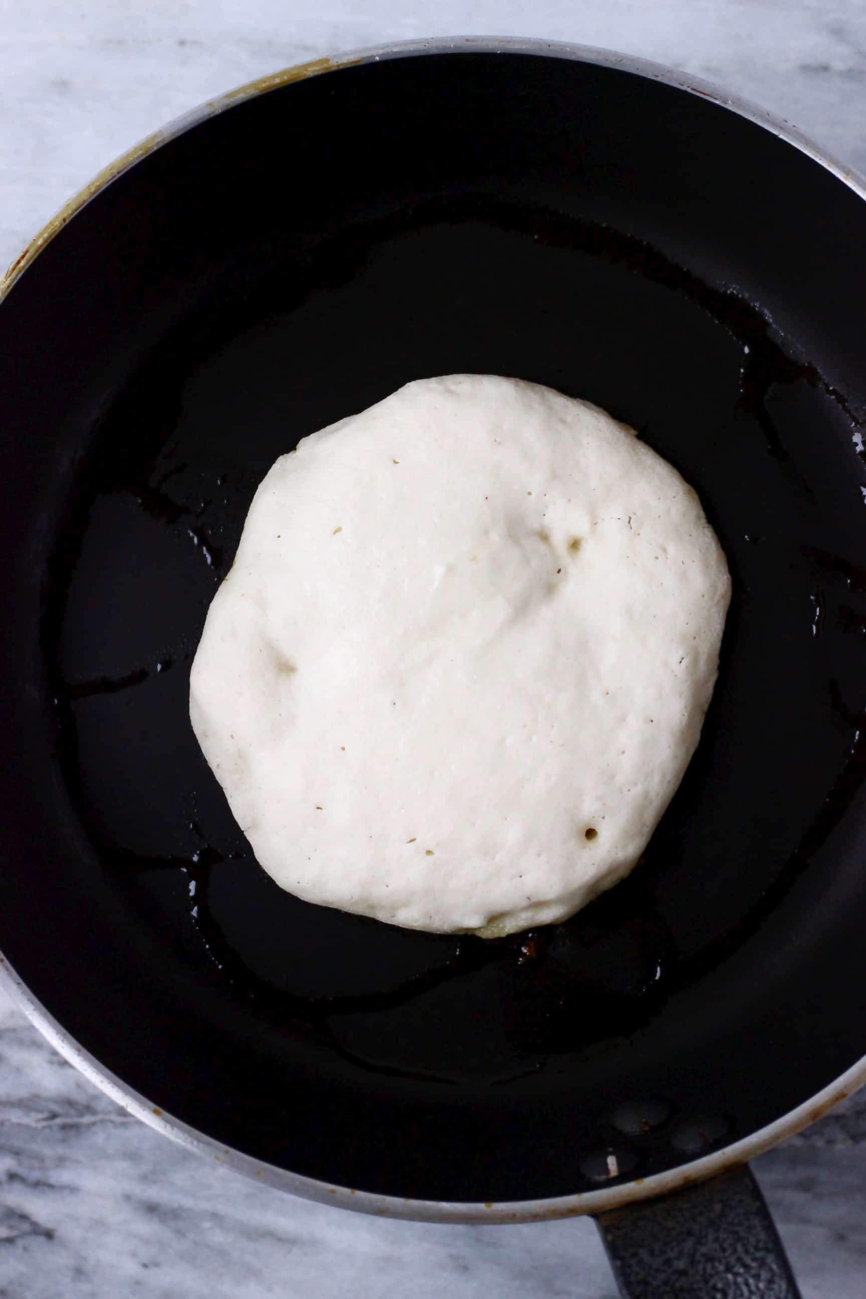 These Gluten-Free Vegan Coconut Flour Pancakes are fluffy, perfectly soft and chewy, and super easy to make. They make the best satisfying and nutritious breakfast! Dairy-free, refined sugar free, egg-free. #rhiansrecipes #pancakes #glutenfree #vegan #coconutflour #dairyfree A white vegan coconut flour pancake being cooked in a black frying pan