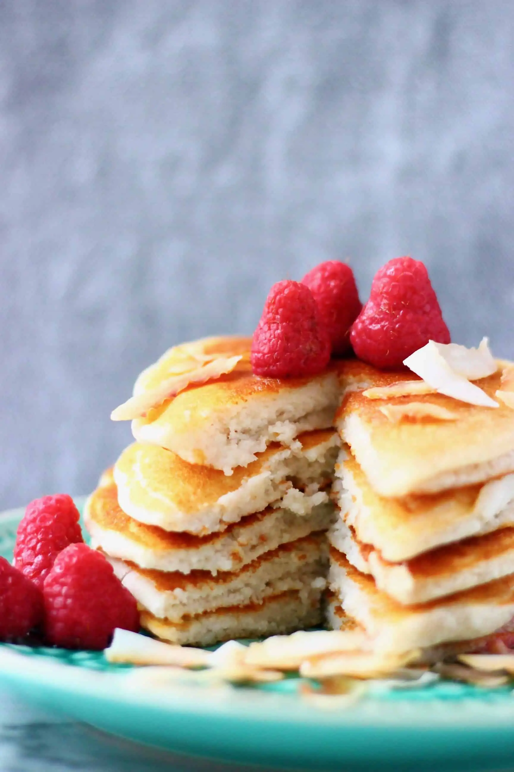 Five vegan coconut flour pancakes stacked in a pile decorated with fresh raspberries on a green plate