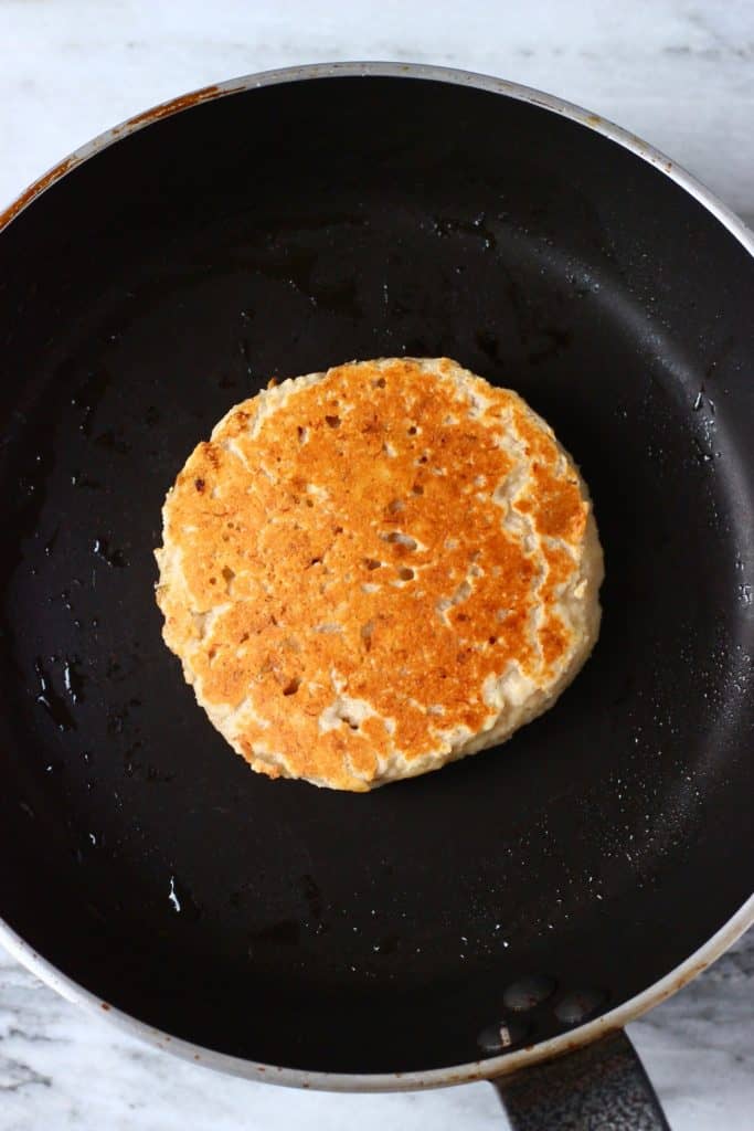 Brown banana pancake in a black frying pan against a marble background