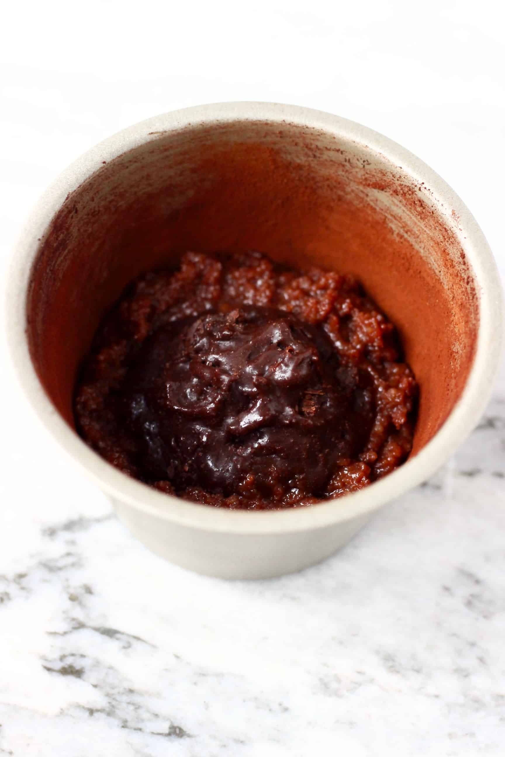 A small silver pudding tin filled with a small amount of raw gluten-free vegan chocolate lava cake batter with a small amount of solid chocolate sauce in the centre 