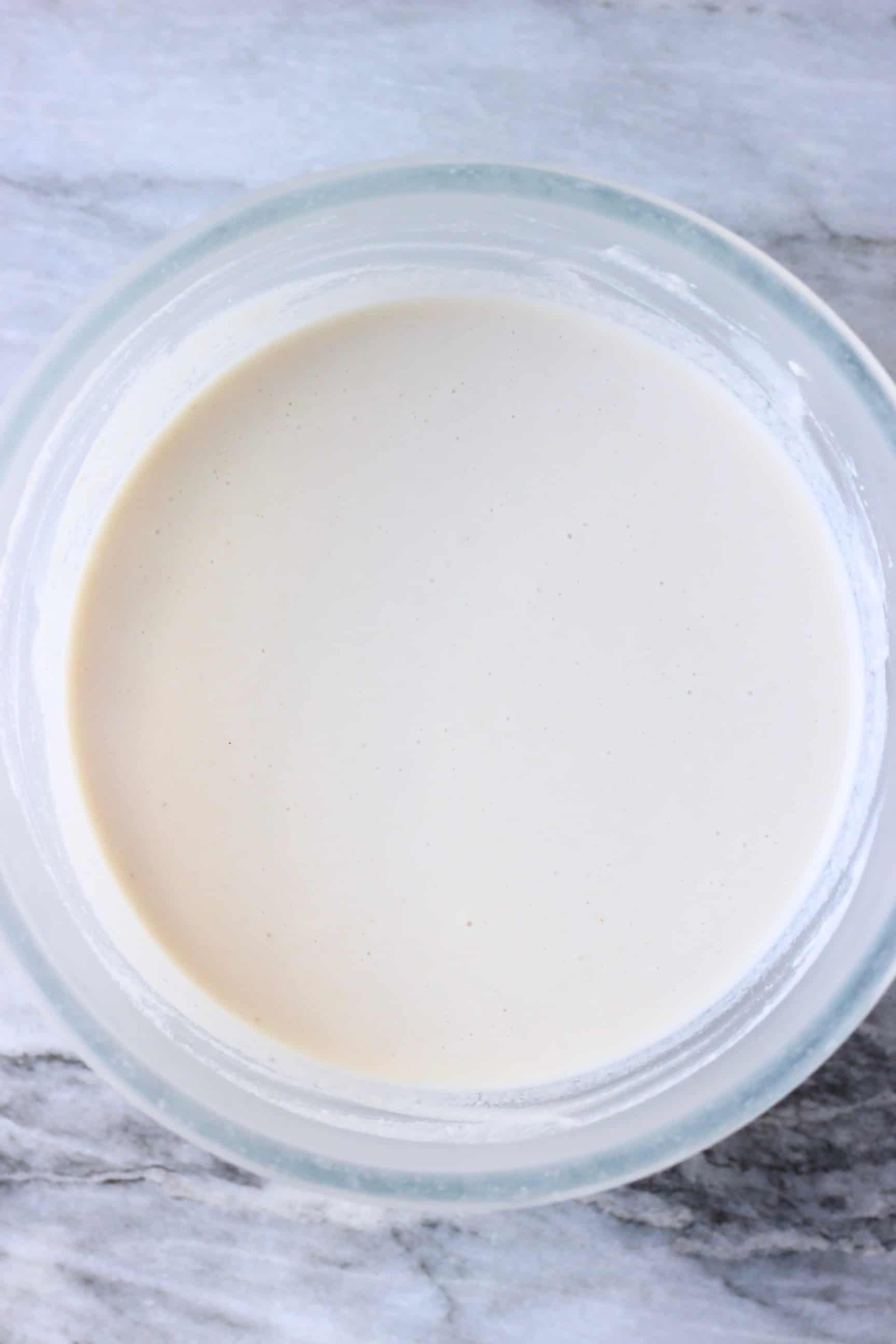 White gluten-free vegan crepes batter in a glass mixing bowl against a marble background