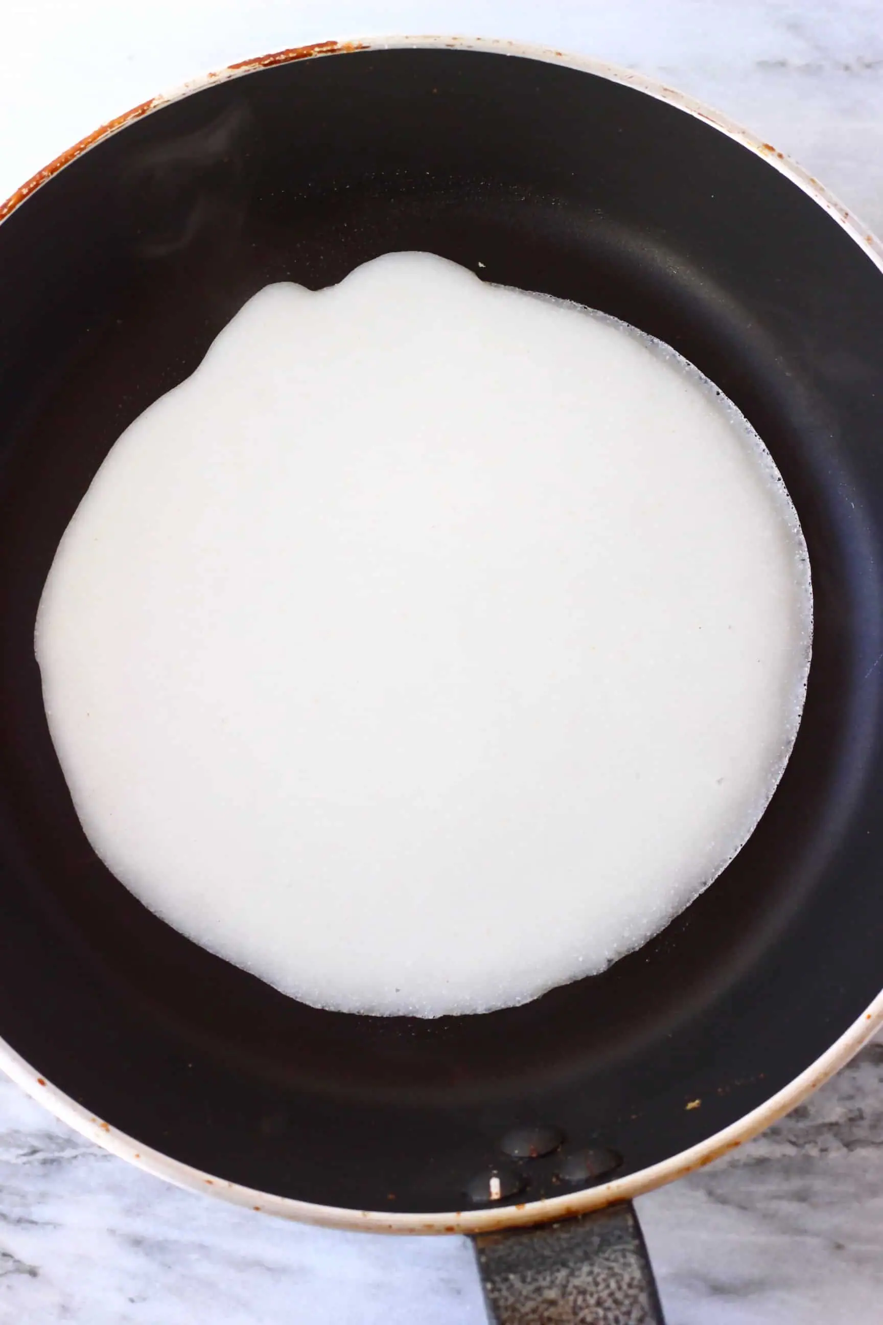 A round gluten-free vegan crepe being fried in a black frying pan 