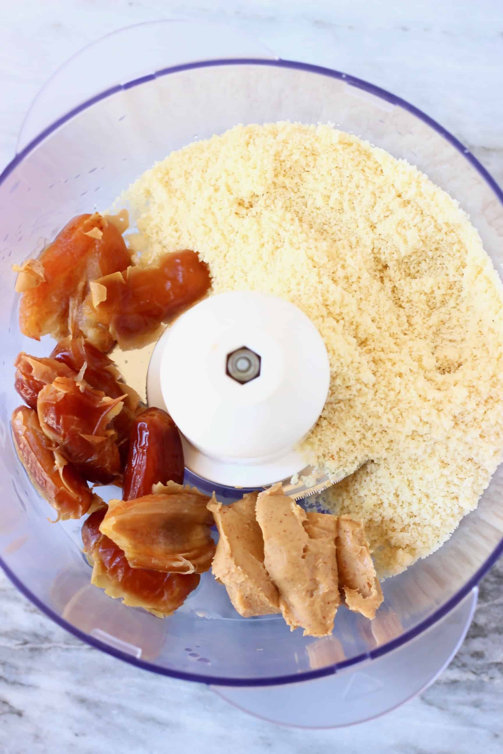 Dates, almond butter and ground almonds in a food processor against a marble background