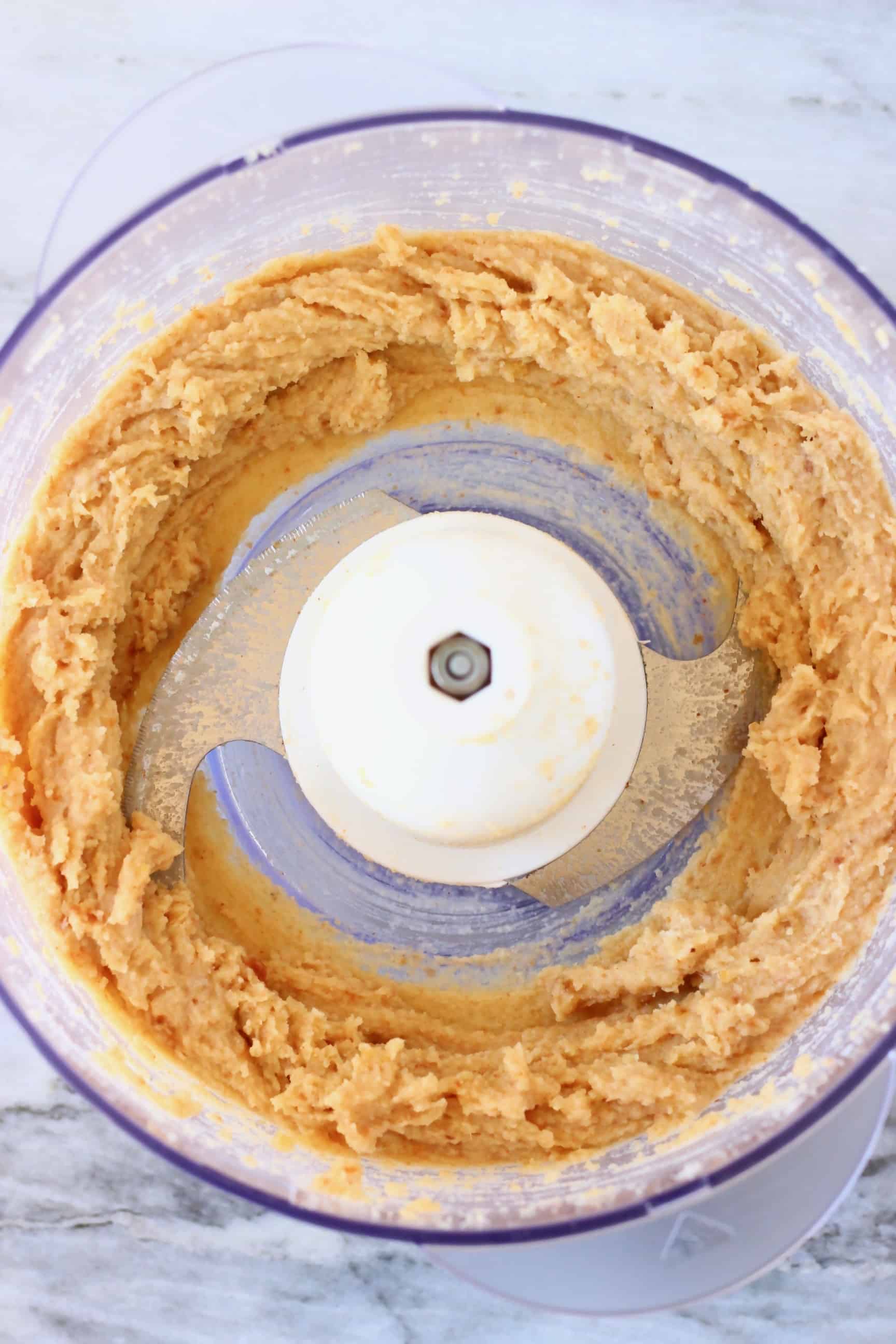 Vegan cookie dough in a food processor against a marble background
