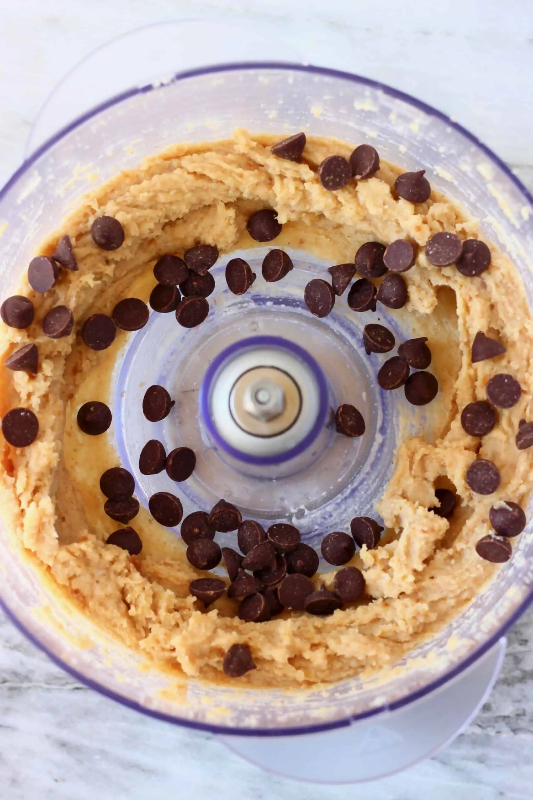 Vegan cookie dough and chocolate chips in a food processor against a marble background