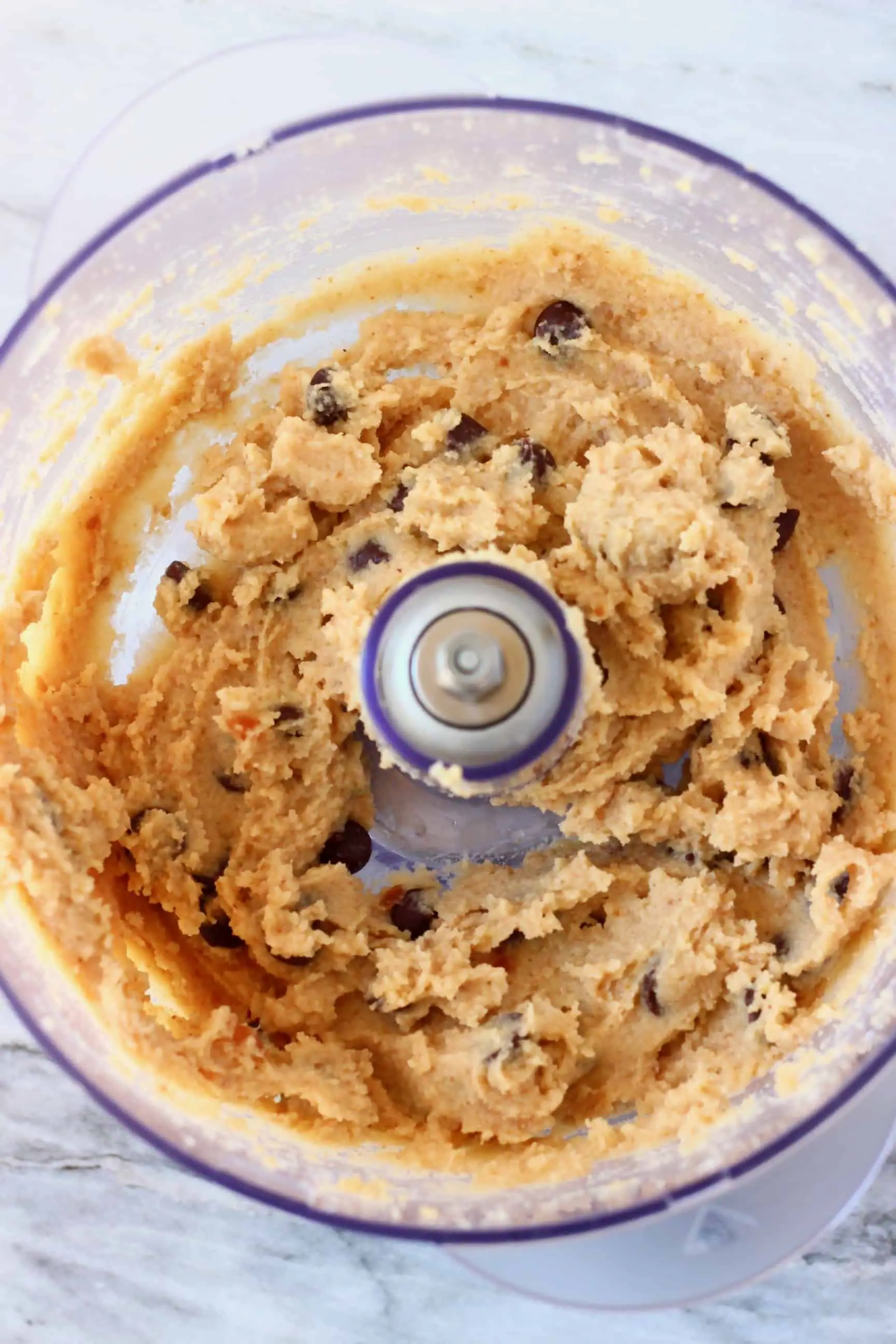 Vegan cookie dough with chocolate chips in a food processor against a marble background