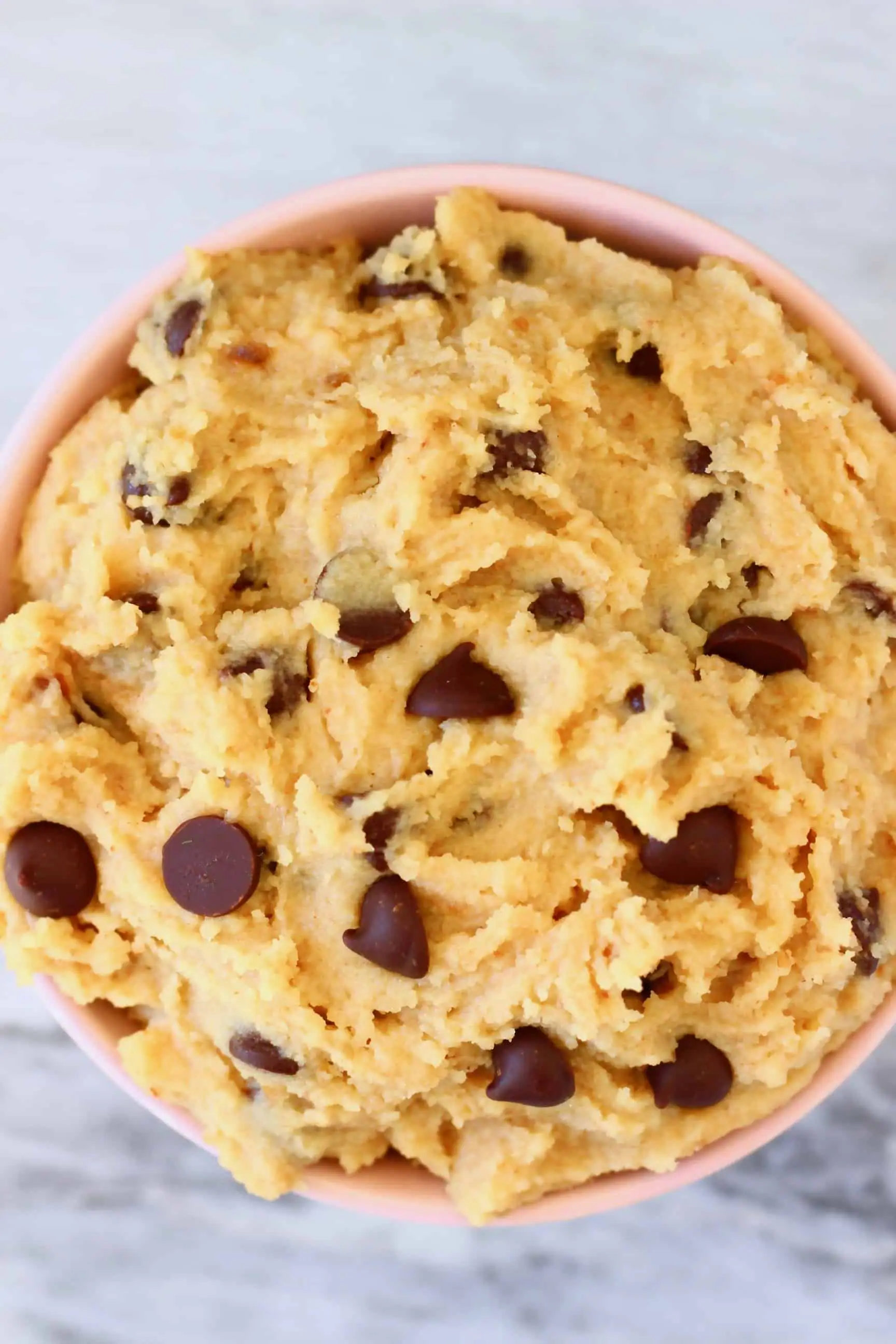 Vegan cookie dough with chocolate chips in a bowl against a marble background