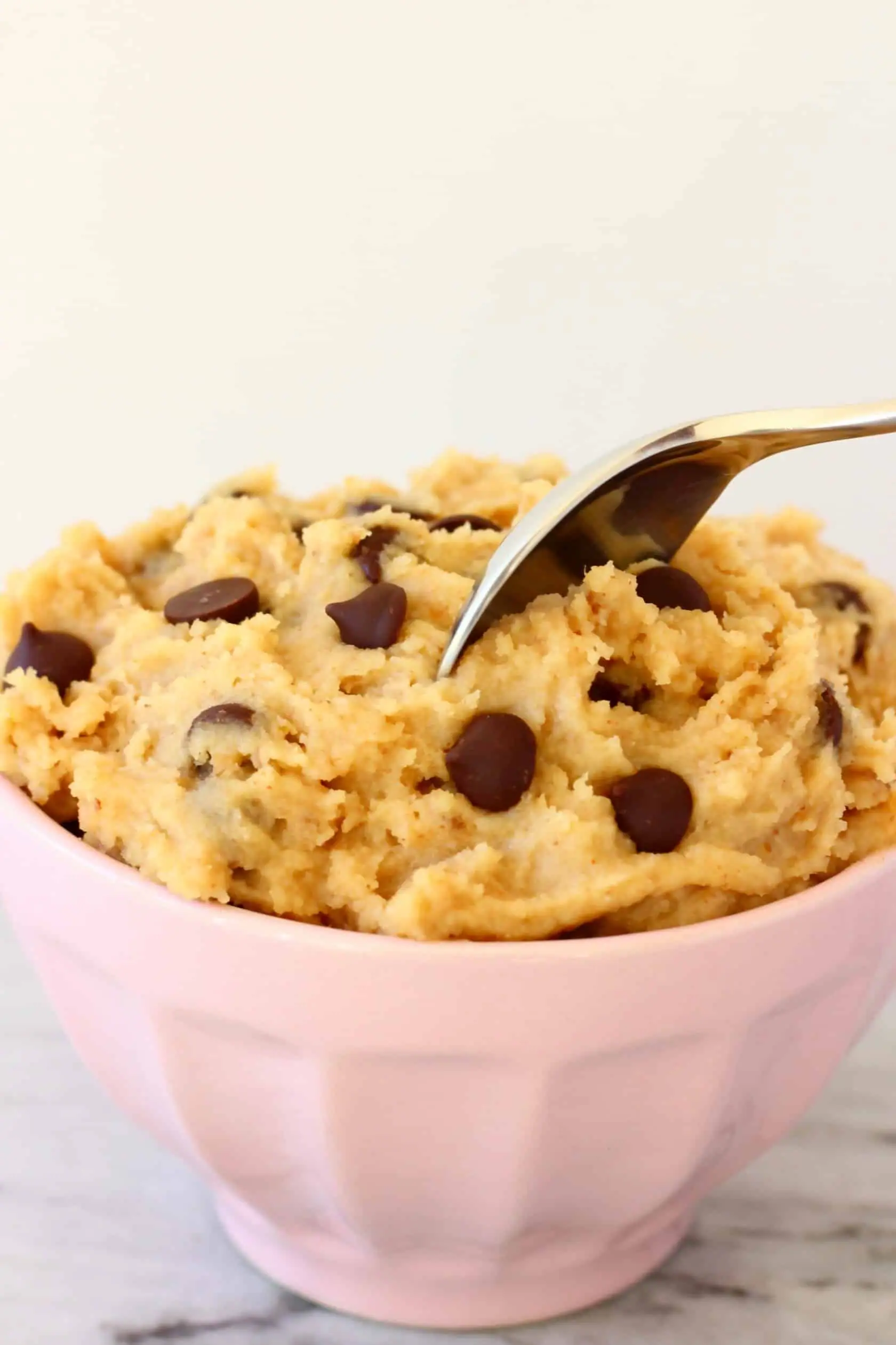 Vegan cookie dough with chocolate chips in a bowl with a spoon sticking into it 
