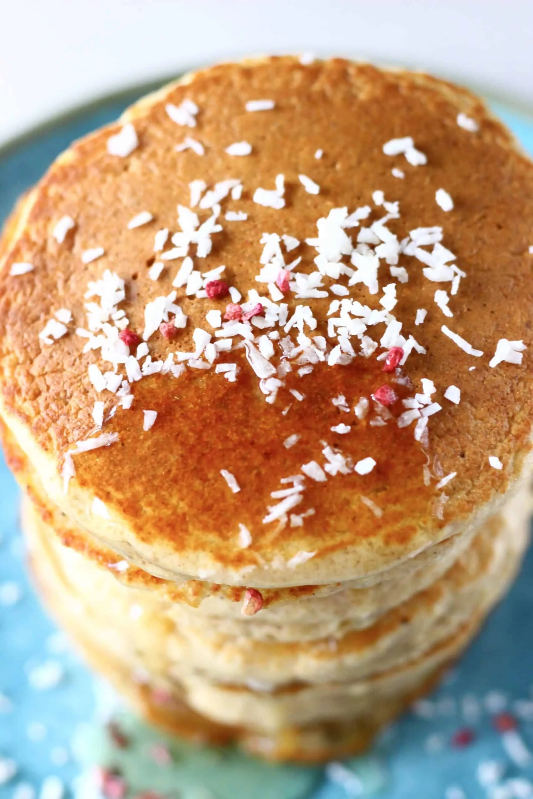 A stack of golden brown pancakes topped with desiccated coconut and syrup on a blue plate