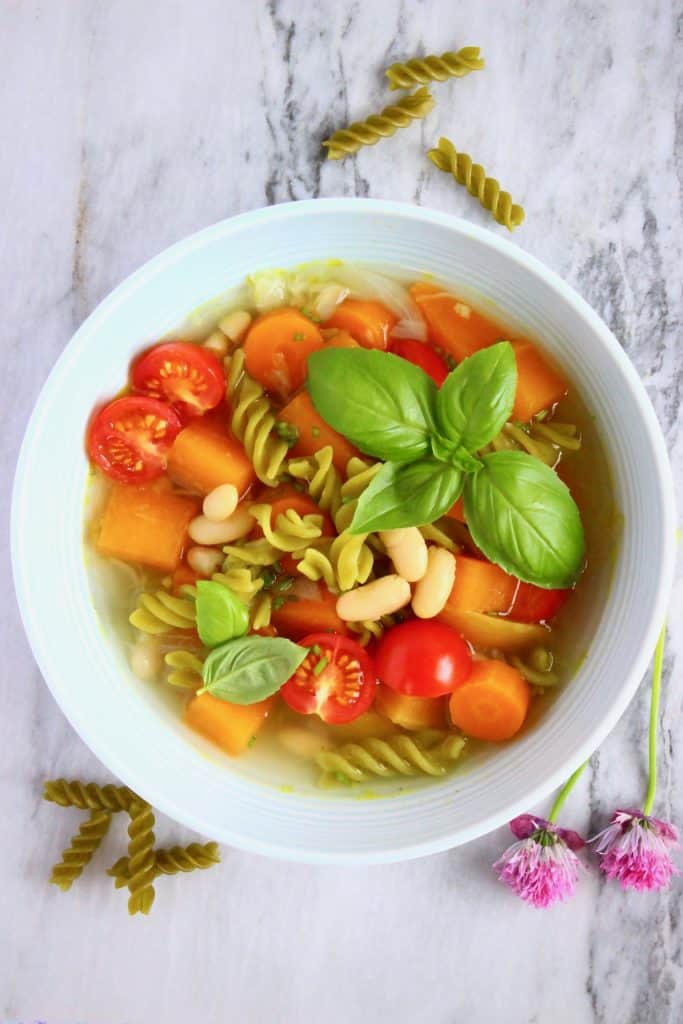 A blue bowl with minestrone with green pea pasta and fresh tomatoes on a marble background